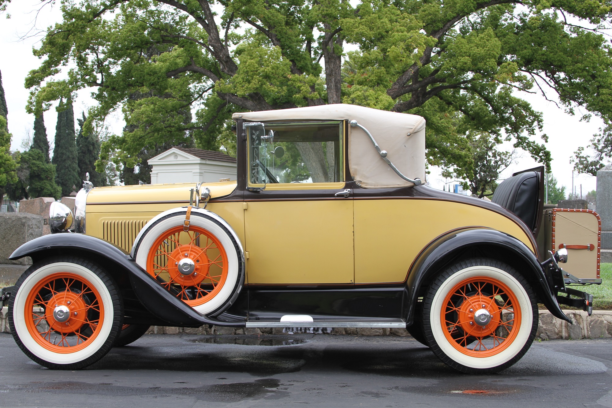 Antique yellow car with orange and white rims in the cemetery